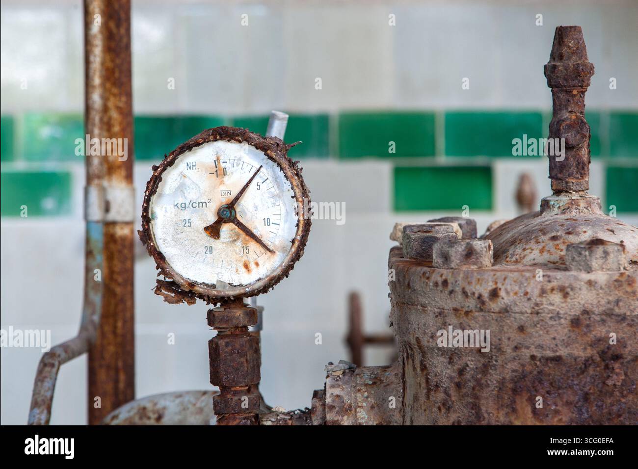 Valvola della pressione arrugginita in una casa di attrezzature abbandonata, un testimone silenzioso della tecnologia passata, segnata da corrosione, polvere e il lento passaggio del tempo. Foto Stock