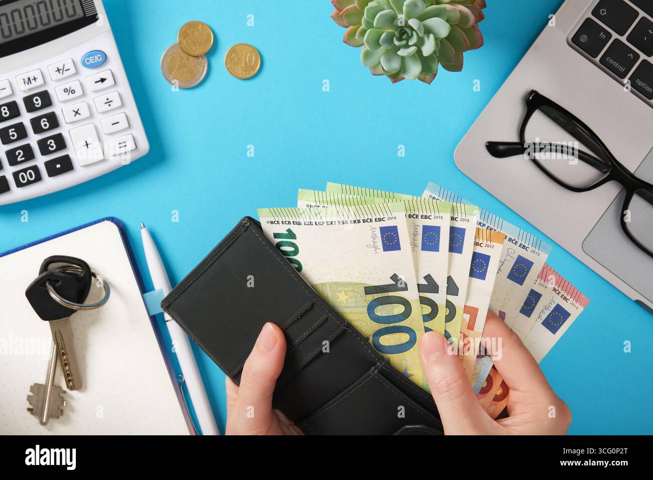Mani che tengono in mano banconote in euro nel portafoglio con calcolatrice, monete, computer portatile e occhiali. Finanza personale e gestione del denaro. Foto Stock