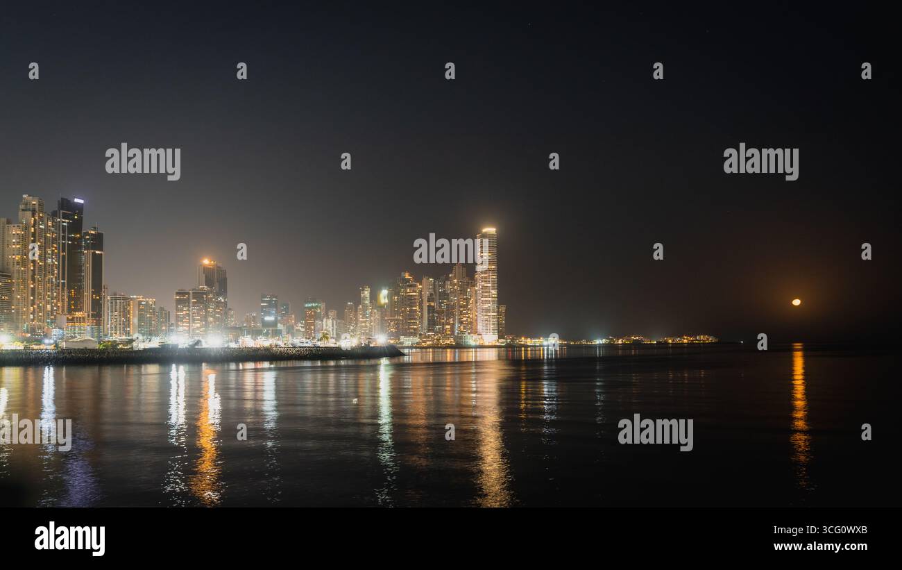 Immagine notturna dello skyline di Panama City con la luna piena che sorge dietro un grattacielo Foto Stock