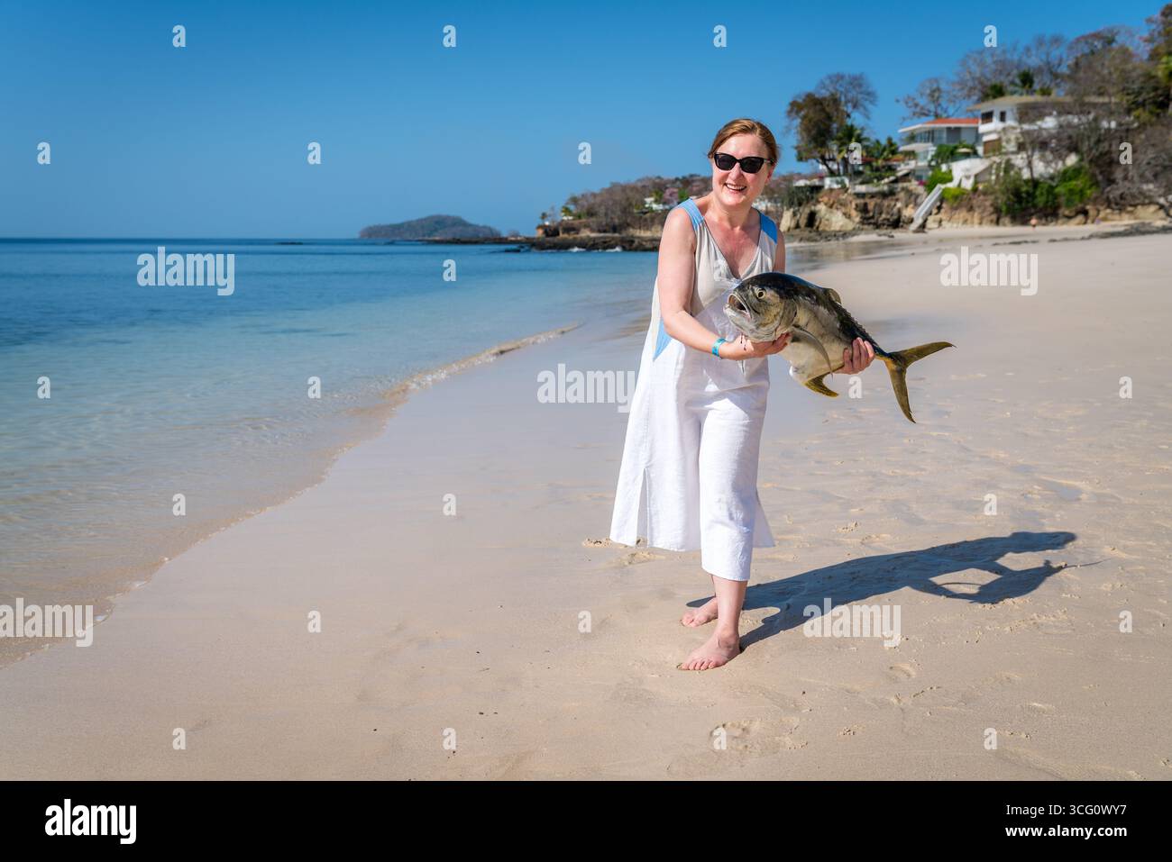 Donna matura felice che mostra pesce appena pescato su una spiaggia di Contadora Island, Panama Foto Stock