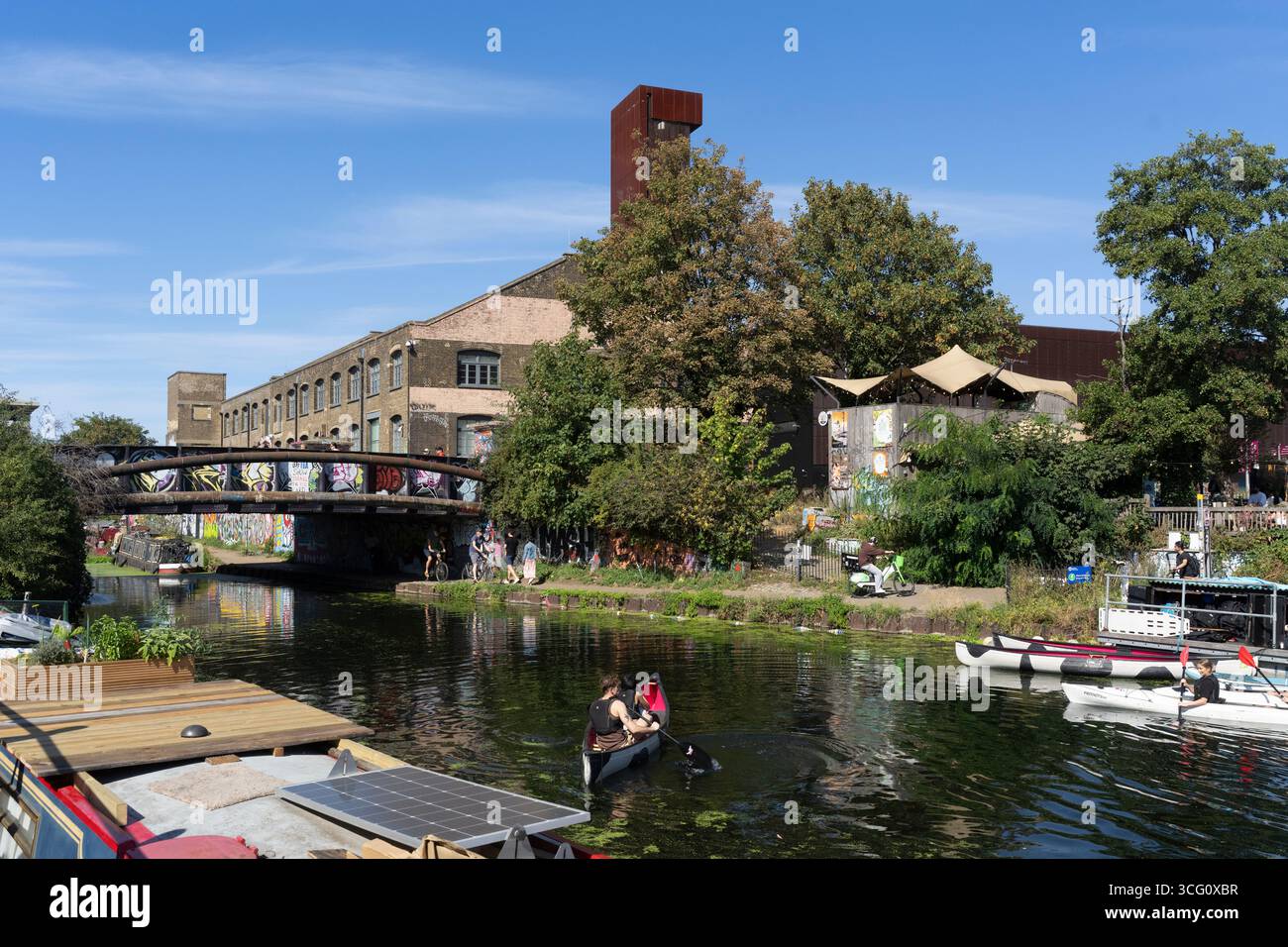 Pagaiando sul Regent's Canal vicino a Hackney Wick, Londra. Sono visibili il ponte coperto di graffiti e la caratteristica torre dell'ex zuccherificio. Foto Stock
