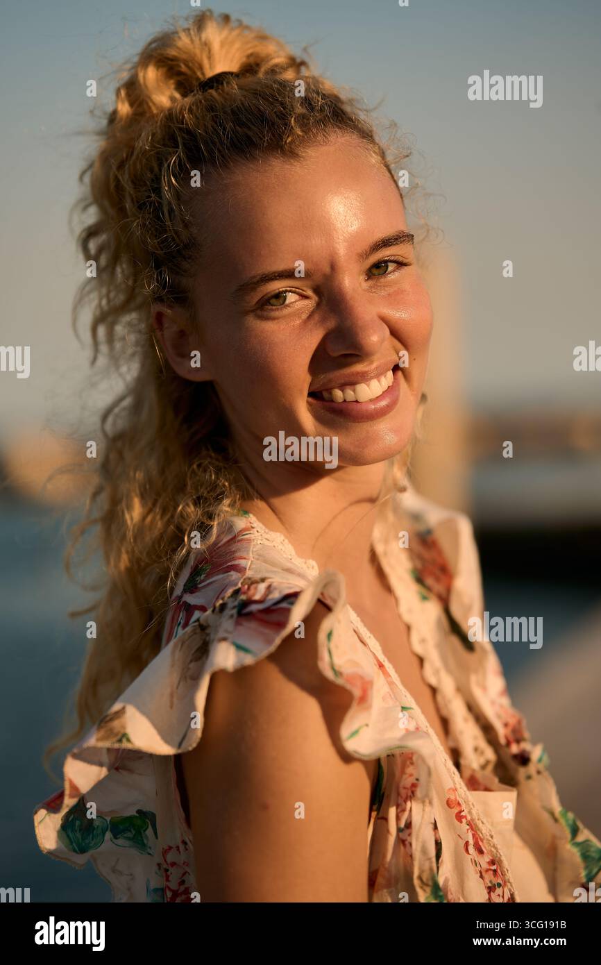 Ritratto di una giovane donna sorridente con capelli biondi ricci al tramonto Foto Stock