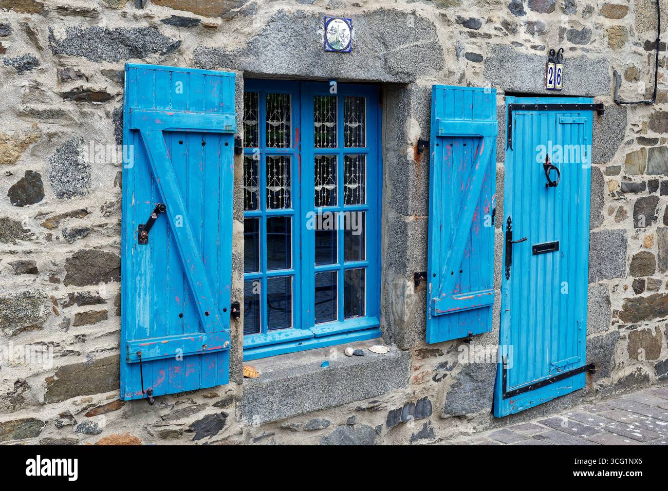 Vecchio cottage di pescatori in pietra naturale con persiane blu e una vecchia porta di legno, Francia, Bretagna, Saint-Quay-Portrieux Foto Stock