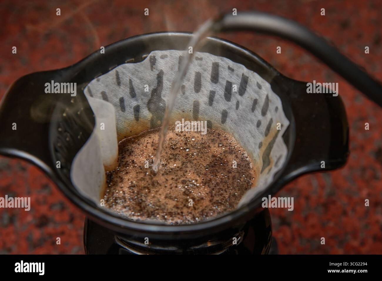 Versamento di acqua calda da un bollitore a collo d'oca in un filtro con caffè macinato, con lievitazione del vapore. Una dose dinamica del metodo di estrazione a pour-over, il capturi Foto Stock