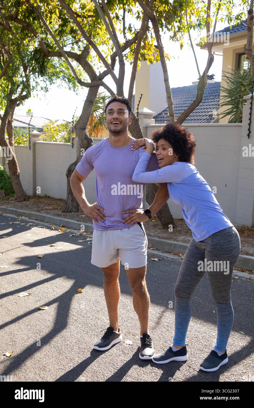 Coppia che fa una pausa in strada suburbana sotto alberi frondosi in abbigliamento sportivo con scarpe da running Foto Stock