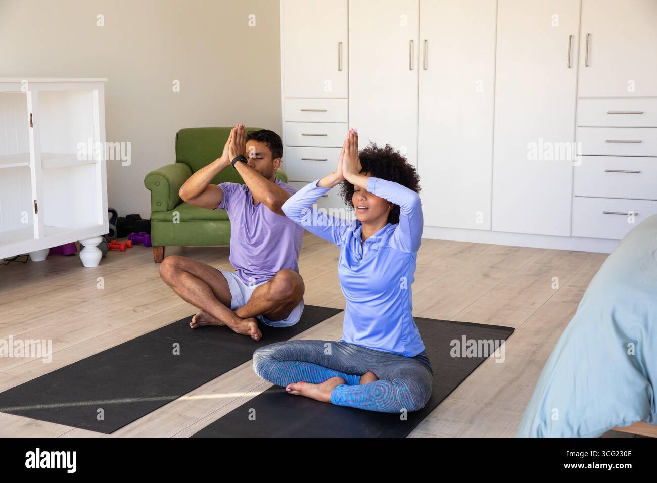 Diversi amici hanno le zampe incrociate su tappetini da yoga neri nello spazio per gli esercizi domestici con manubri Foto Stock