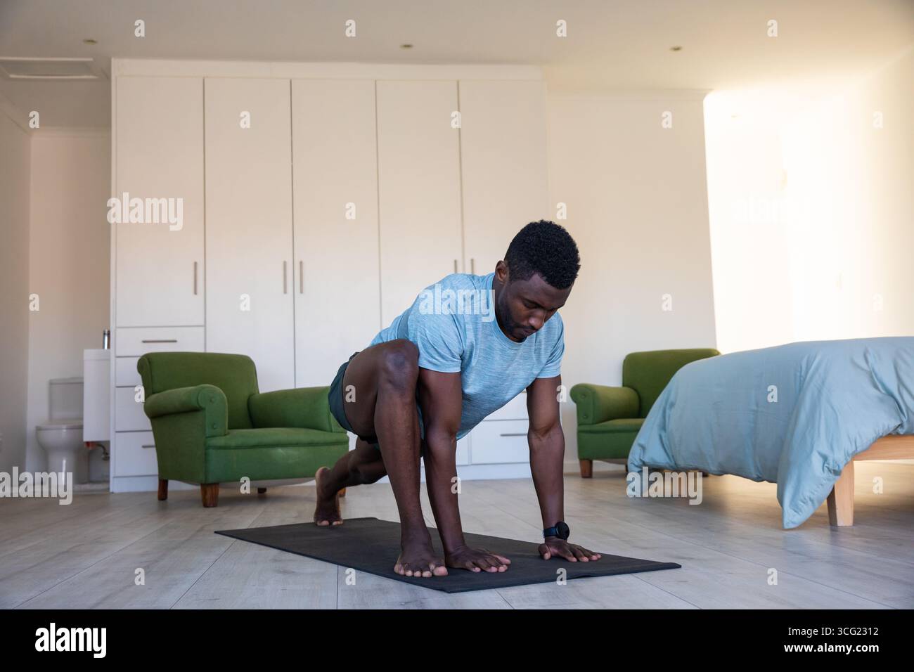 Uomo afroamericano medio adulto in abbigliamento atletico che si estende su un tappeto nero in camera da letto Foto Stock