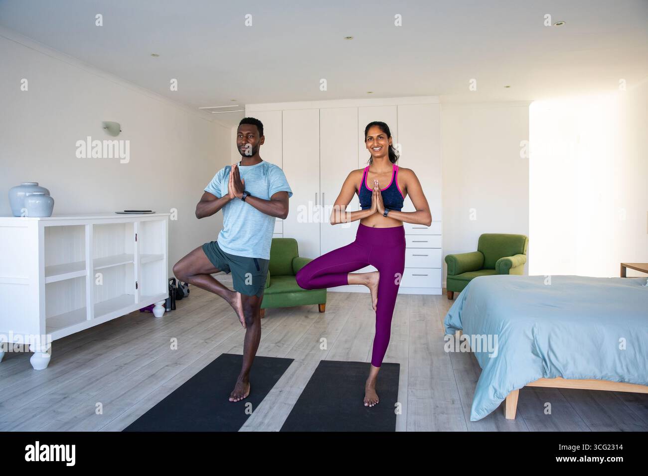 Coppia afroamericana che pratica posa sugli alberi su tappeti neri in camera da letto con comò e vasi Foto Stock