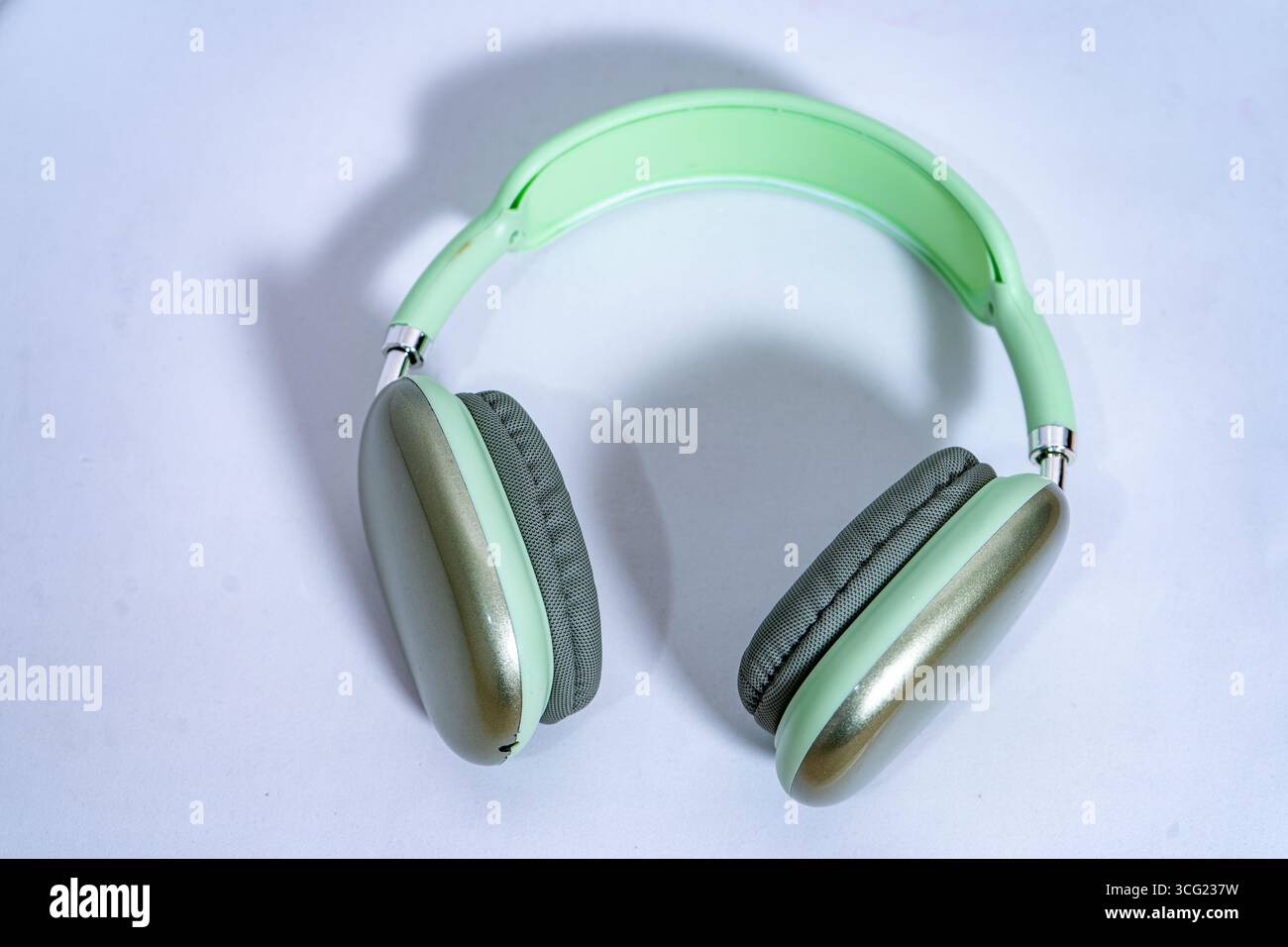 Eleganti cuffie wireless color verde pastello poggiate su una superficie bianca e pulita, che rappresentano musica, tecnologia e divertimento audio Foto Stock