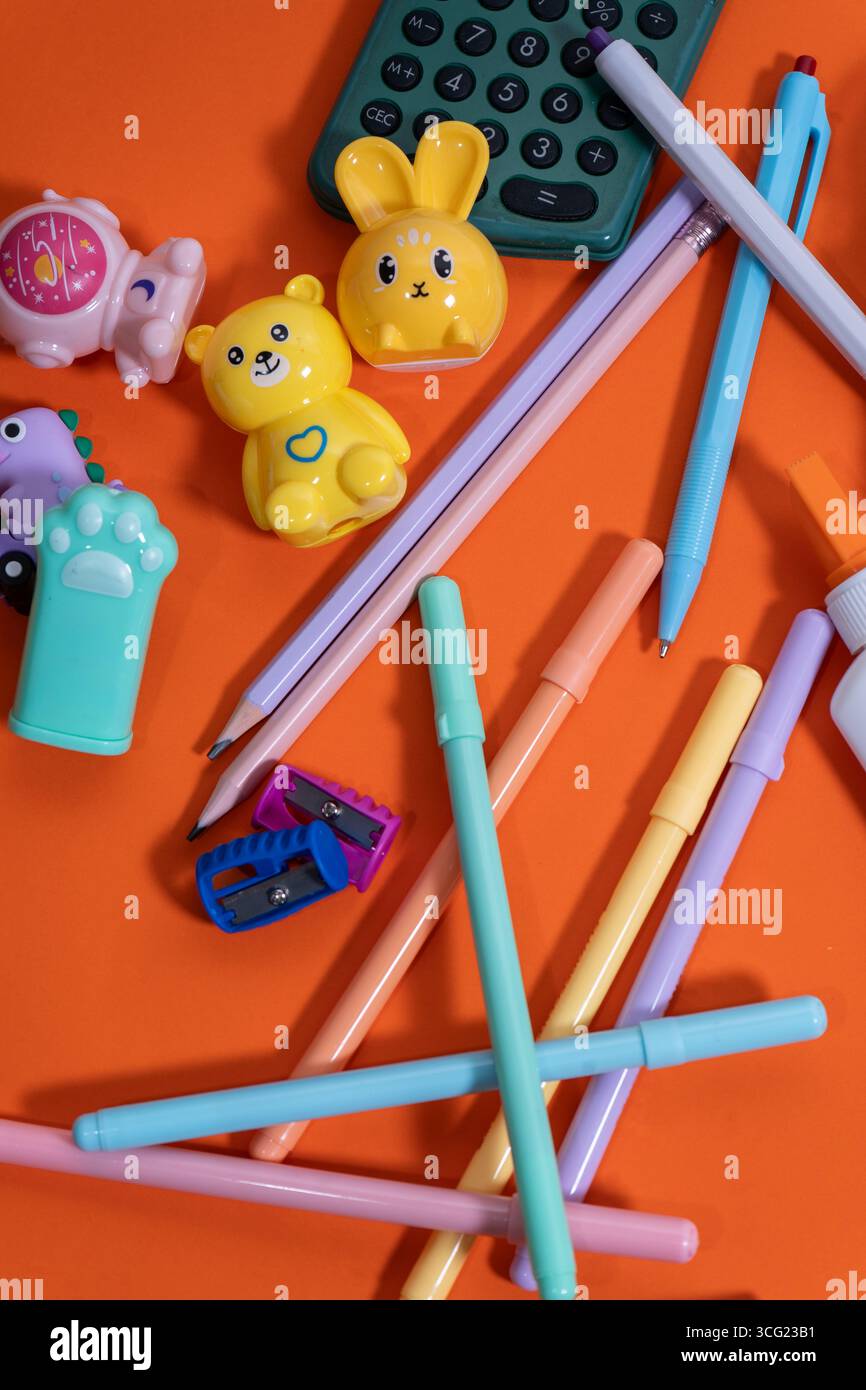 Penne color pastello, matite, gomme, affilatrici e una calcolatrice creano un'allegra scena di ritorno a scuola su un vivace sfondo arancione Foto Stock