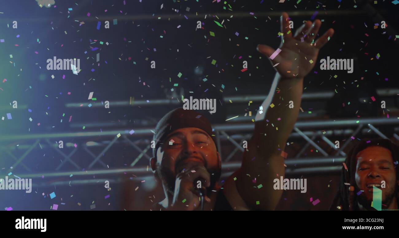 Cantante che indossa bandana e tiene il microfono e alza la mano sul palco, con coriandoli Foto Stock