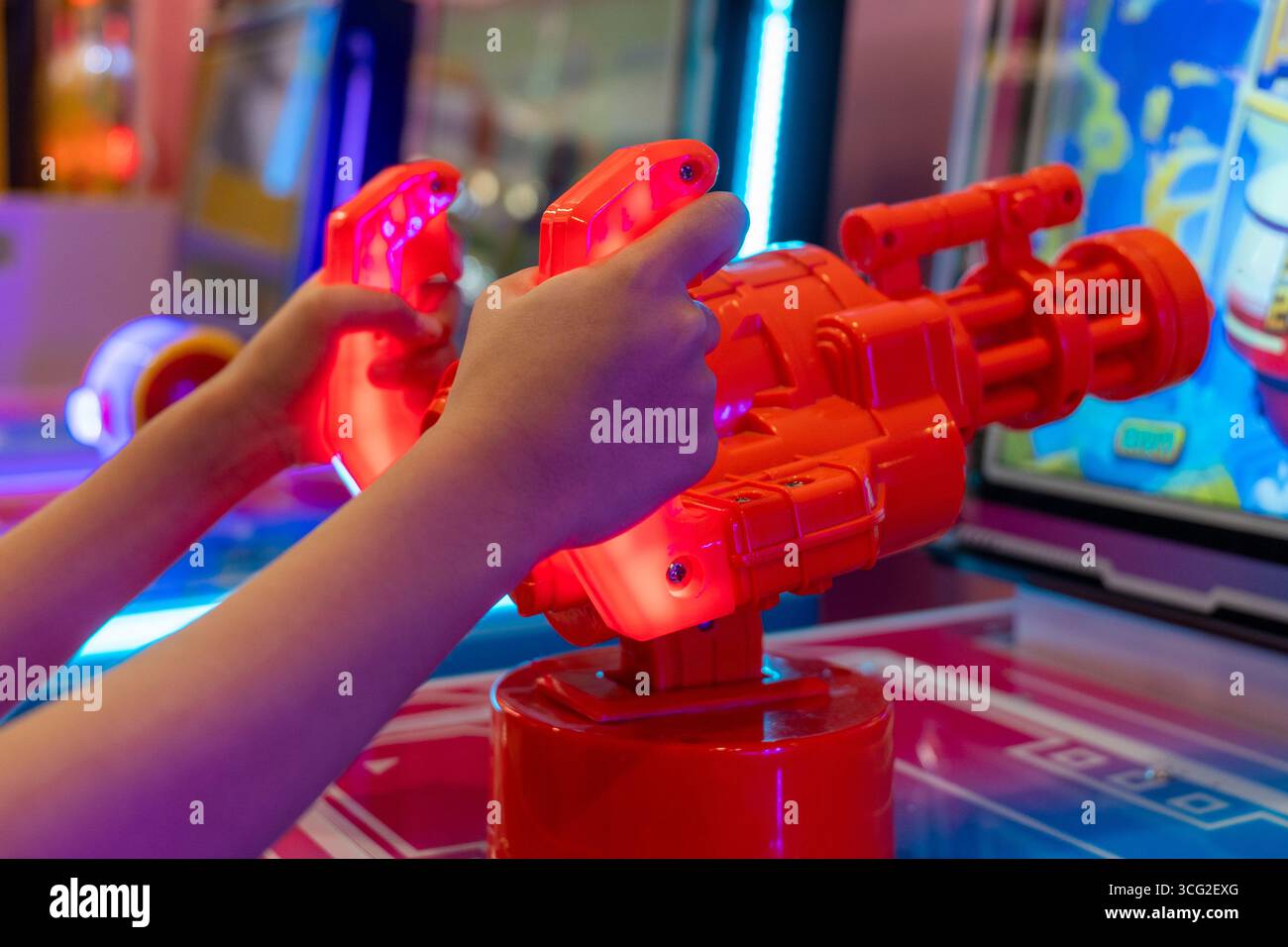 Primo piano di una mano che regge una pistola giocattolo rossa dall'aspetto futuristico di un gioco arcade. L'emozione e l'azione di giocare a un videogame in una sala giochi Foto Stock