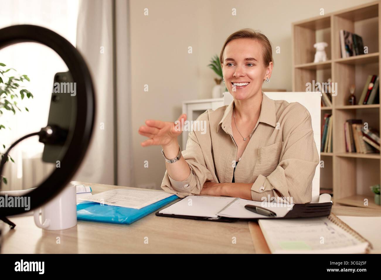 Una donna professionista comunica durante una riunione online in un ufficio domestico. Seduta a una scrivania, parla con un sorriso, trasudando fiducia e profezia Foto Stock