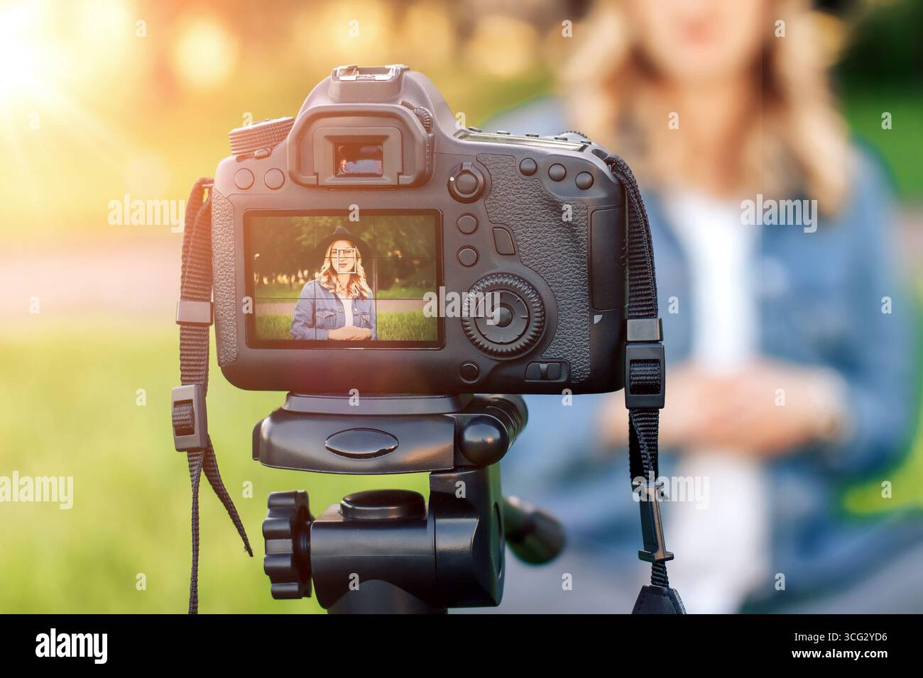 La giovane blogger elegante seduto sull'erba davanti alla telecamera e scatta video. Giovane donna bionda che lavora come blogger registrando video tutorial Foto Stock