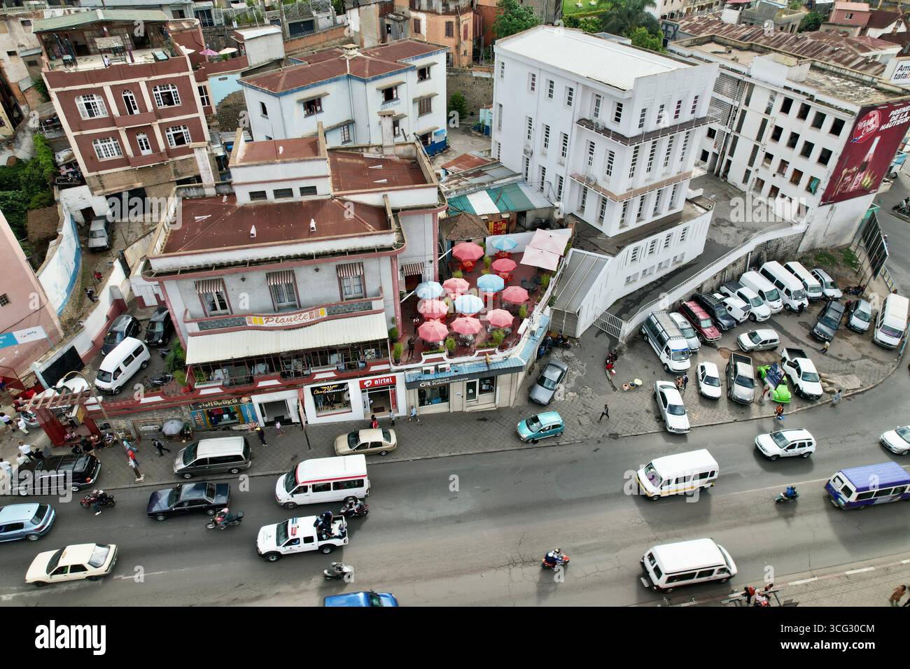 Antananarivo (TNR), Madagascar – 2023/11/09: Veduta aerea degli ombrelli sul tetto di Planète Terrasse sopra l’arteria di transito di Ambohijatovo con taxi e motos Foto Stock