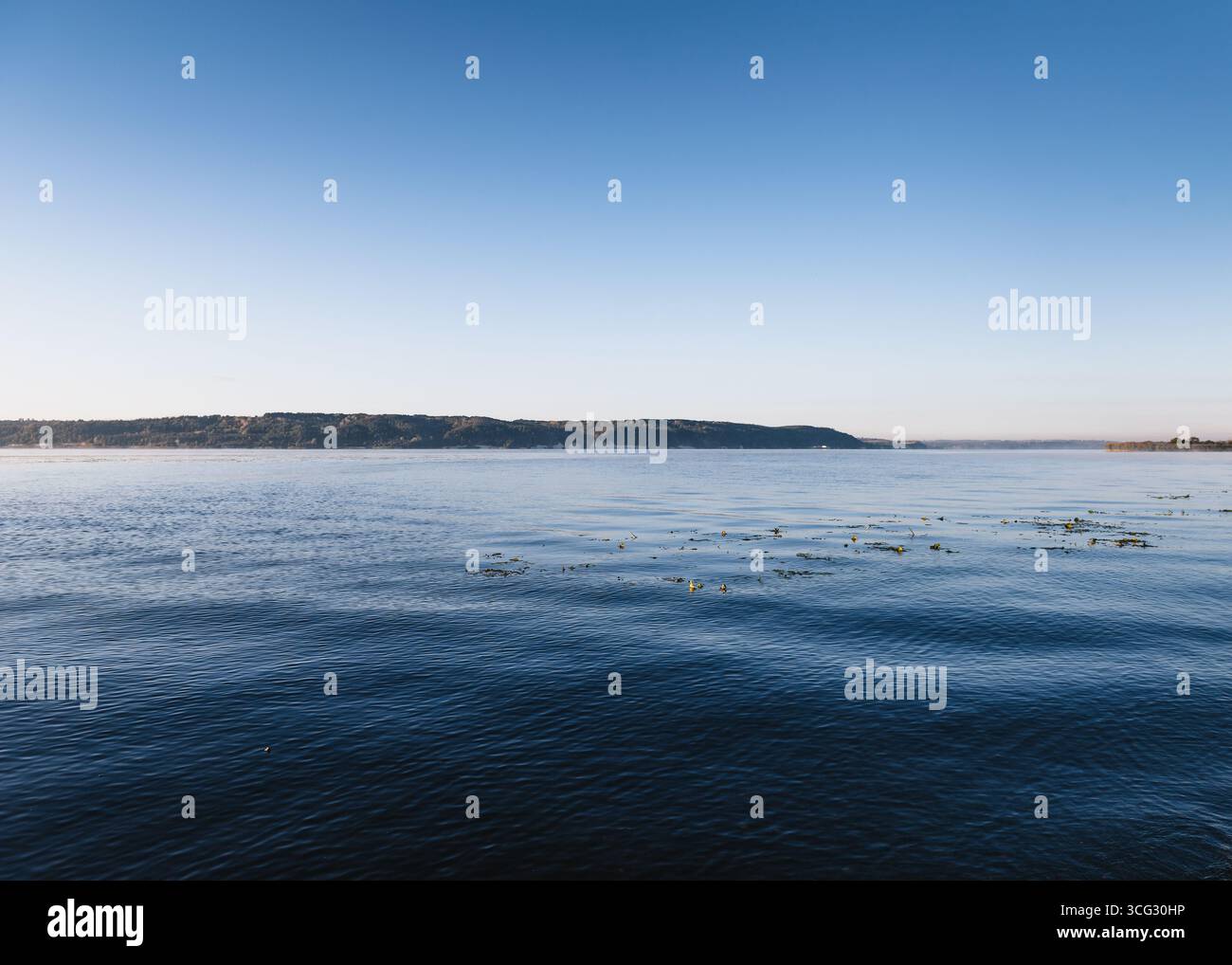 Lago in mattinata. Macchina fotografica vicino alla superficie dell'acqua calma del grande lago poco dopo l'alba. Cielo in pendenza sopra la riva montana del fiume. Foto Stock