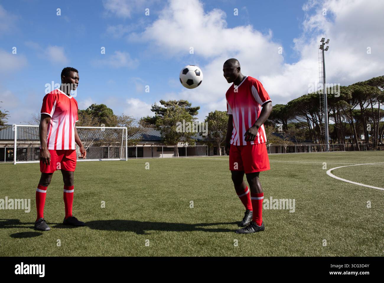 Compagni di squadra afroamericani in divise rosse che si dirigono a pallone da calcio sul campo vicino al punto di accesso, alla torre faro Foto Stock