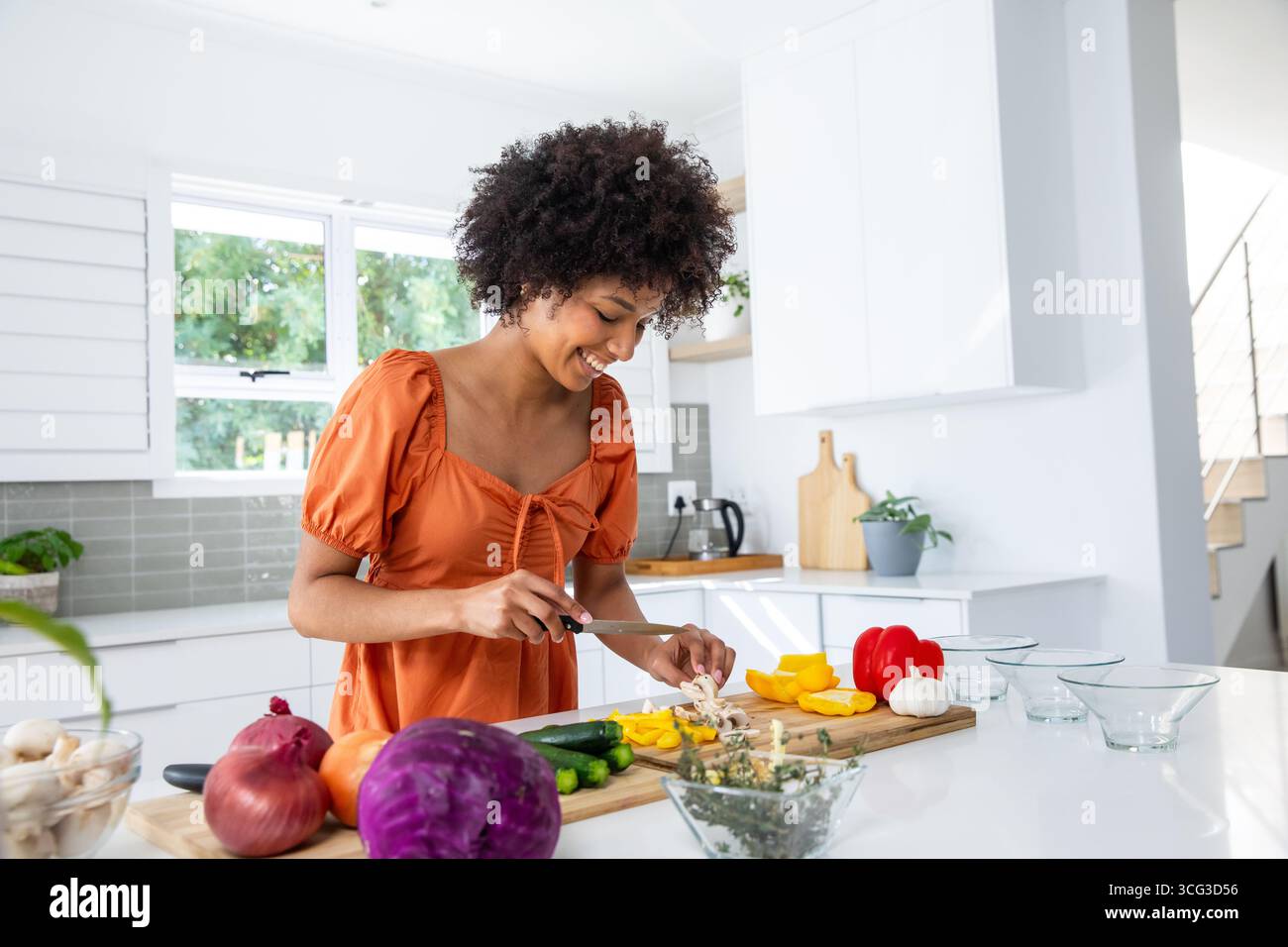 Donna afroamericana che affetta i funghi sul tagliere a Kitchen Island Foto Stock