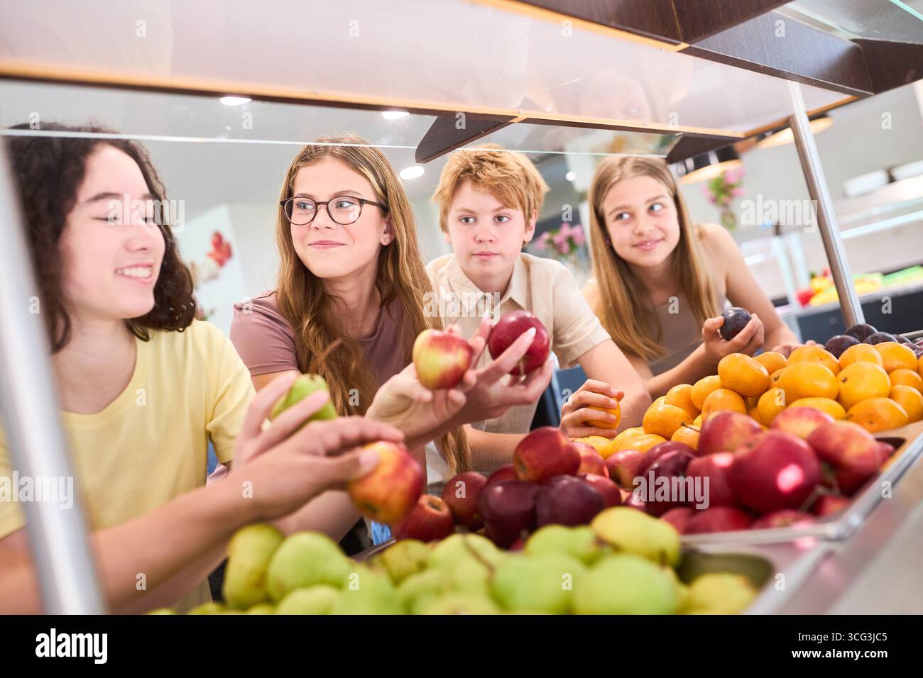 Un gruppo di studenti sceglie frutta fresca in una caffetteria scolastica, promuovendo un'alimentazione sana. Foto Stock