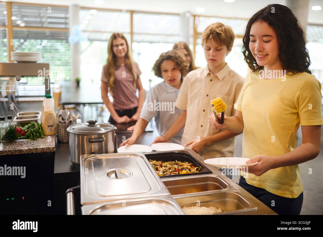 Gli studenti fanno la fila per pranzare in una caffetteria della scuola, che serve pasti freschi. L'atmosfera è allegra e la caffetteria è pulita e organizzata, creat Foto Stock