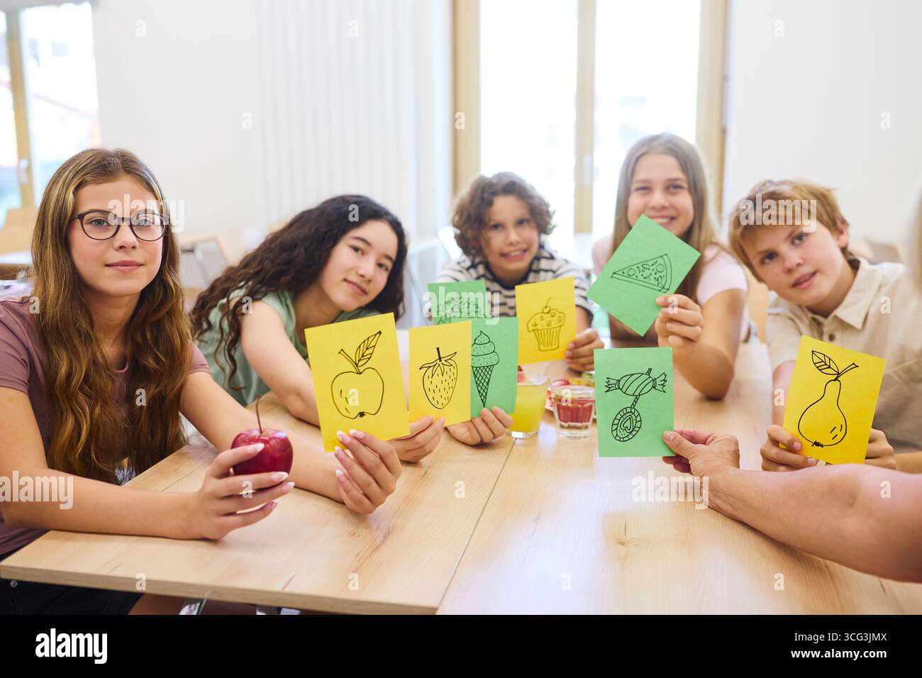 Un allegro gruppo di scolari in una caffetteria che regala disegni colorati a tema alimentare, promuovendo un'alimentazione sana e la creatività. L'ambientazione mostra Foto Stock