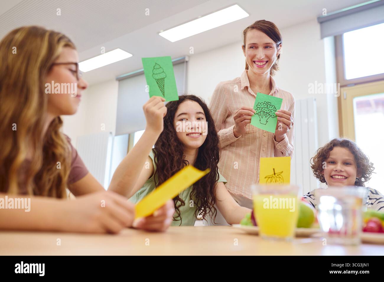 Un insegnante accanto agli studenti in una classe, che mostra illustrazioni colorate, promuove l'apprendimento e l'interazione durante un'attività educativa. BRI Foto Stock