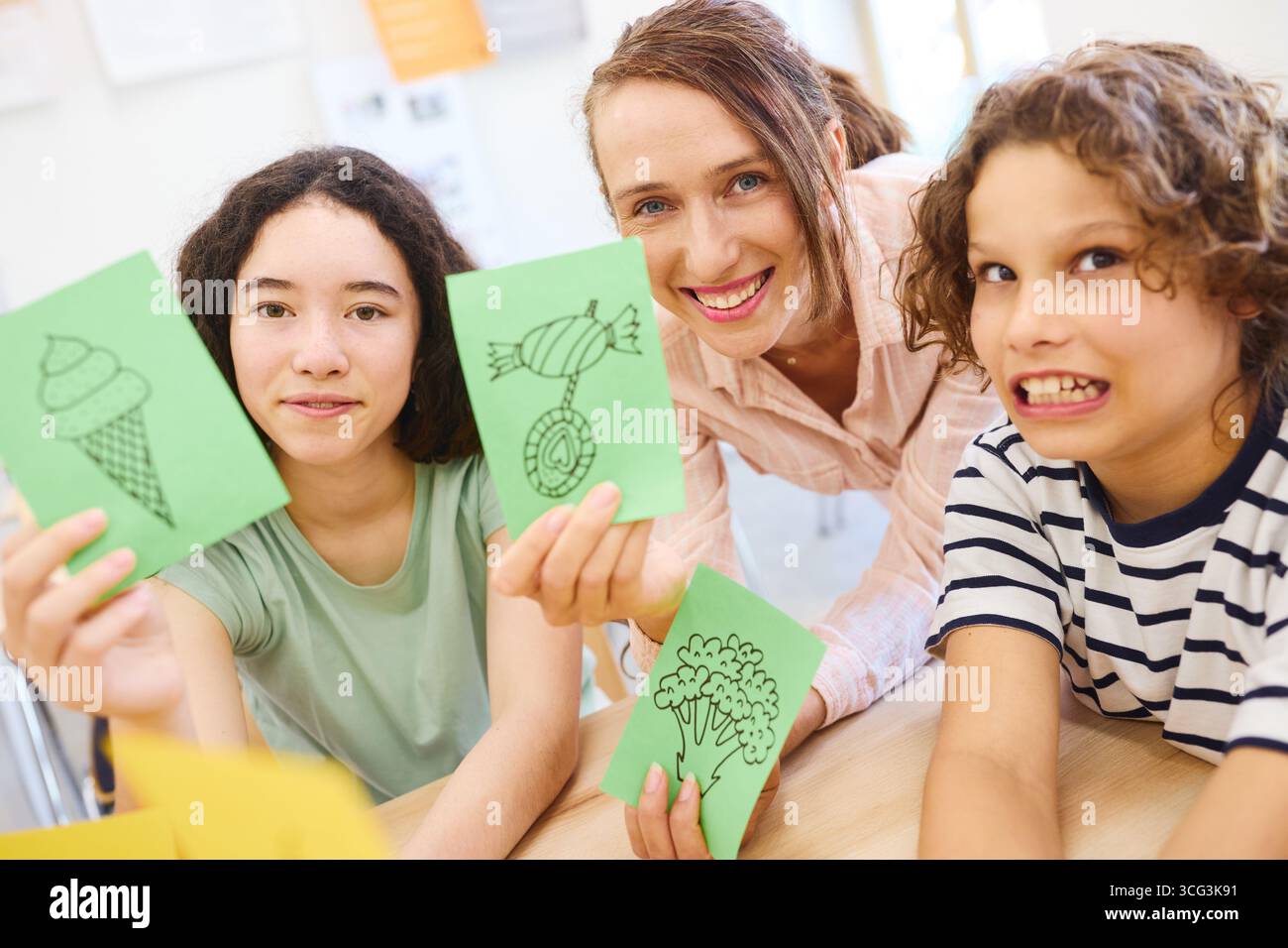 Un insegnante con due studenti che espone disegni di cibi in un ambiente educativo. Foto Stock