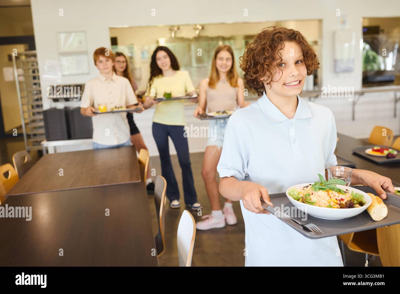 Gruppo di studenti in una mensa scolastica con vassoi con opzioni alimentari salutari. La scena mostra un'atmosfera accogliente, pasti diversi e pulito Foto Stock
