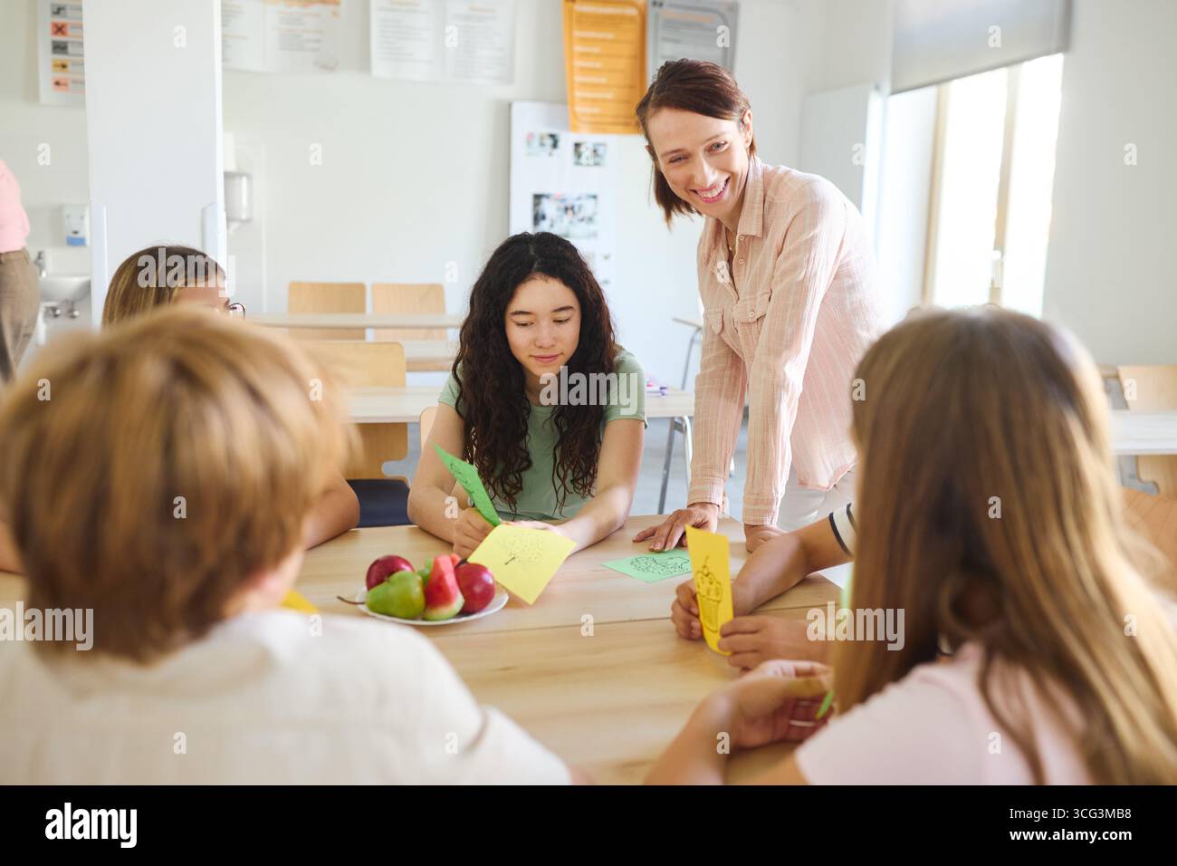 Un insegnante impegnato con gli studenti che partecipano a un'attività didattica artigianale in una caffetteria scolastica. I prodotti freschi vengono messi sul tavolo, favorendo Foto Stock
