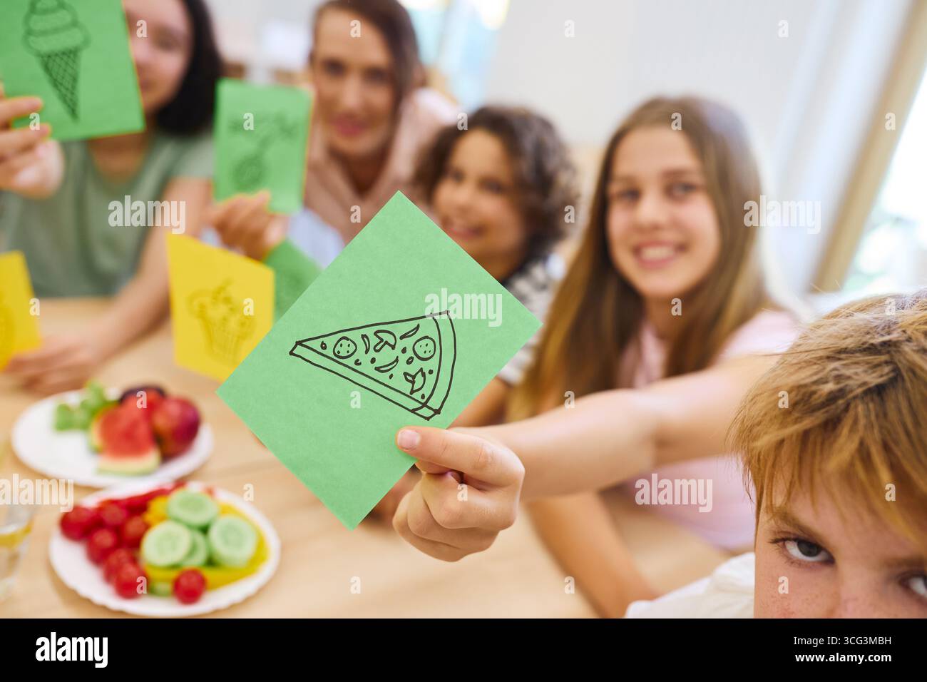 Gruppo di bambini in una mensa scolastica attivamente impegnati tenendo in mano carte legate al cibo, mostrando il loro interesse per un'alimentazione sana e la creatività Foto Stock