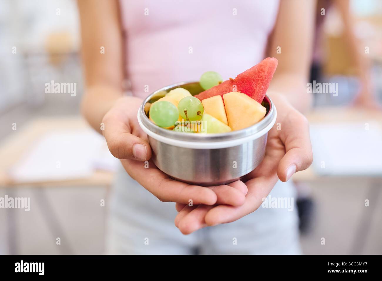 Un individuo tiene una ciotola di pezzi di frutta dai colori vivaci e tagliati al momento in un'atmosfera informale, che riflette l'attenzione su spuntini sani e un vivace ed edu Foto Stock