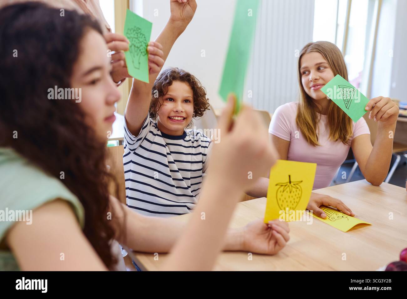 Gruppo di scolari impegnati in un'attività interattiva in classe incentrata sull'apprendimento di temi alimentari. Ambiente luminoso e cooperativo Foto Stock