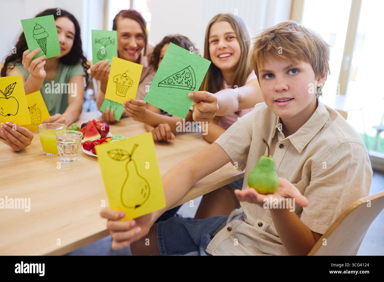 Un gruppo di studenti impegnati in un'attività, tenendo in mano carte con disegni di cibo in una caffetteria scolastica. Foto Stock