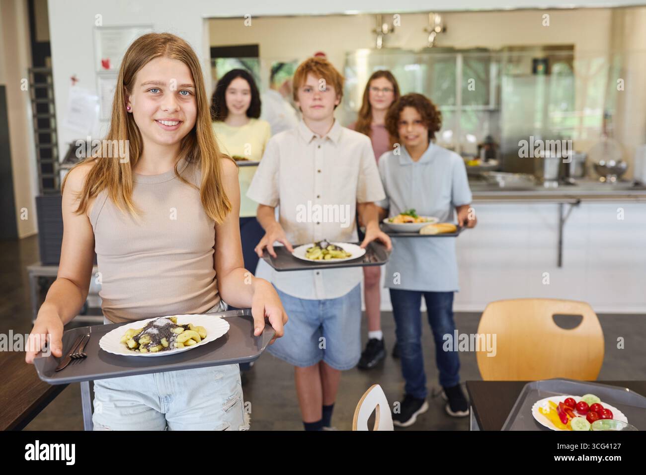 Un gruppo di adolescenti raccoglie pasti nutrienti in una caffetteria scolastica organizzata e pulita. Foto Stock