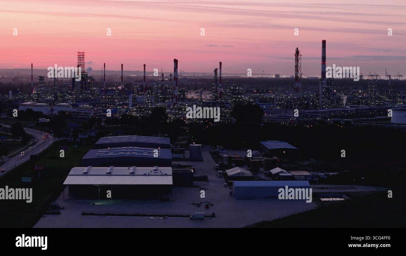 Panorama aereo al crepuscolo di una massiccia raffineria di petrolio e un impianto petrolchimico vicino a un porto marittimo, che rappresenta l'industria pesante, il settore energetico e il glob Foto Stock