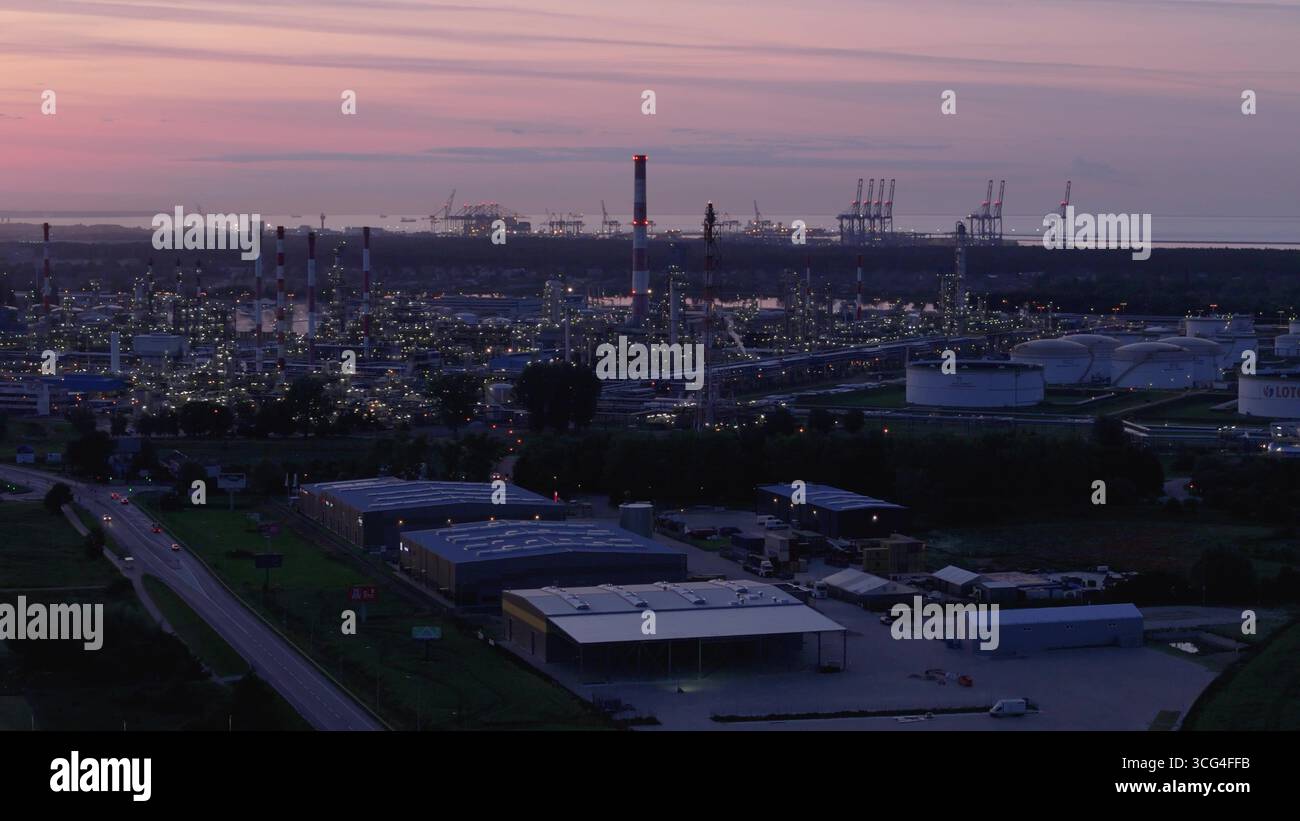 Panorama aereo al crepuscolo di una massiccia raffineria di petrolio e un impianto petrolchimico vicino a un porto marittimo, che rappresenta l'industria pesante, il settore energetico e il glob Foto Stock