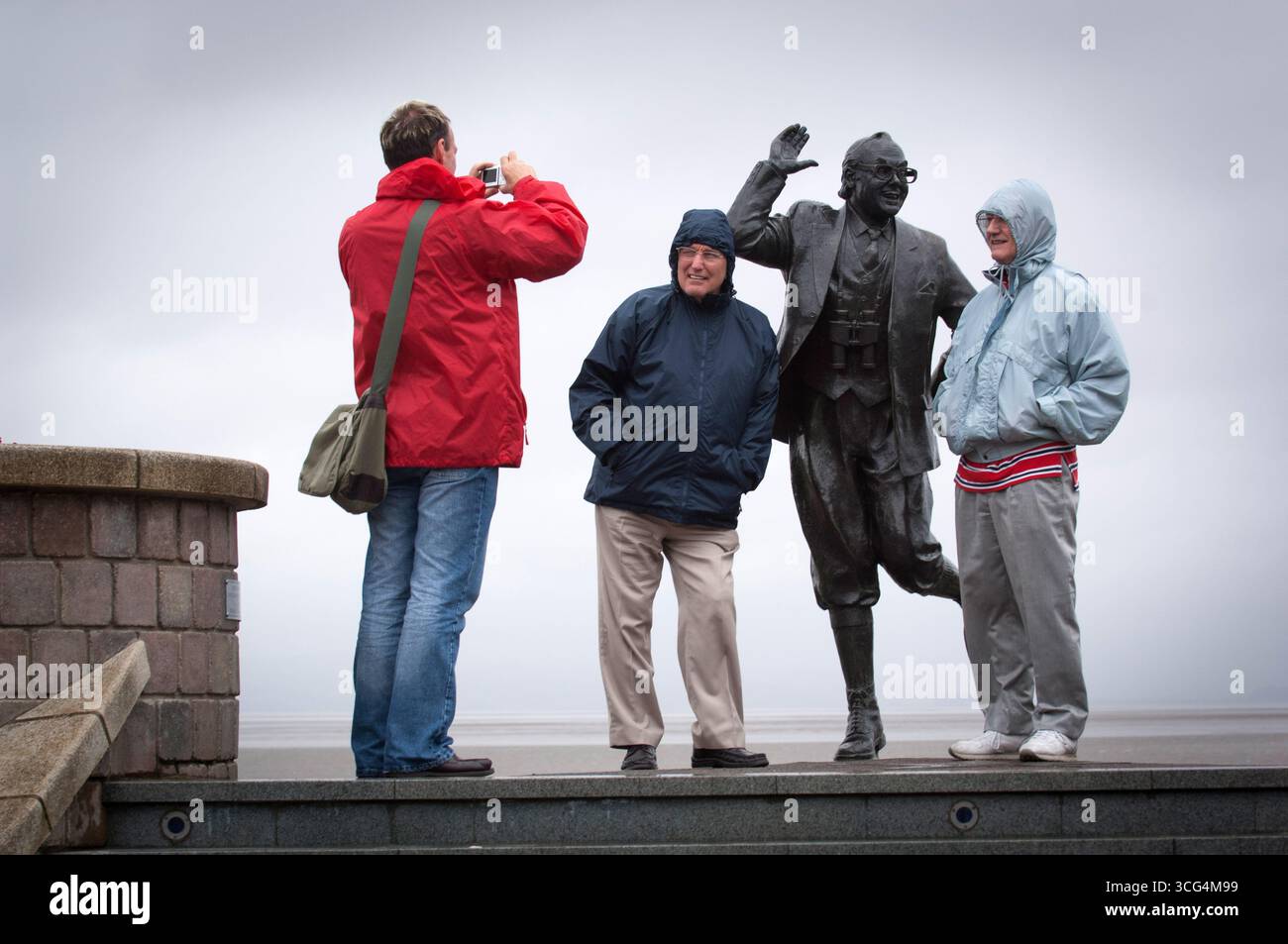 Due turisti si posano per una fotografia presso la statua a grandezza naturale che raffigura Eric Morecambe a Morecambe Bay, Lancashire, Regno Unito. Foto Stock