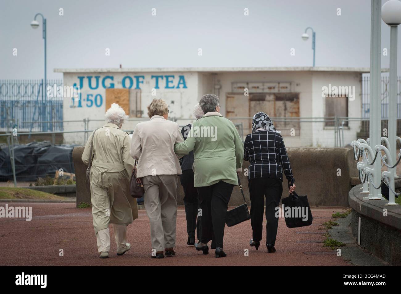 I pensionati hanno fatto una passeggiata in una giornata umida e ventosa a Morecambe Bay, Lancashire, Regno Unito Foto Stock