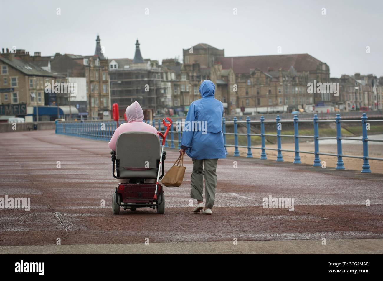 I pensionati hanno fatto una passeggiata in una giornata umida e ventosa a Morecambe Bay, Lancashire, Regno Unito Foto Stock