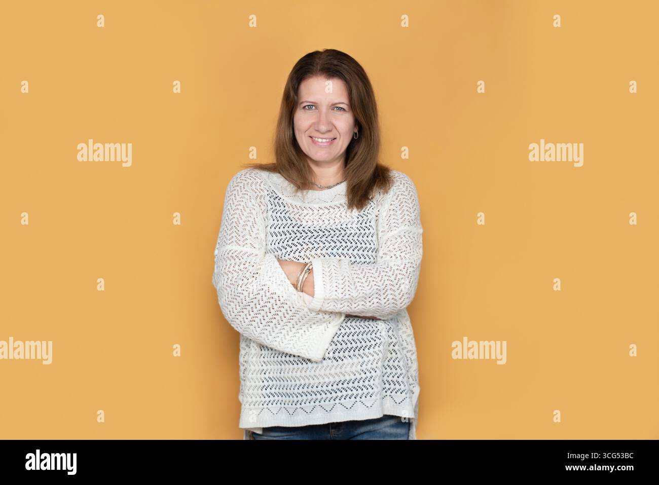 Ritratto di una donna di mezza età, sorridente e sicura, con le braccia incrociate, trasmessa da un caldo sfondo arancione ed espressiva Foto Stock
