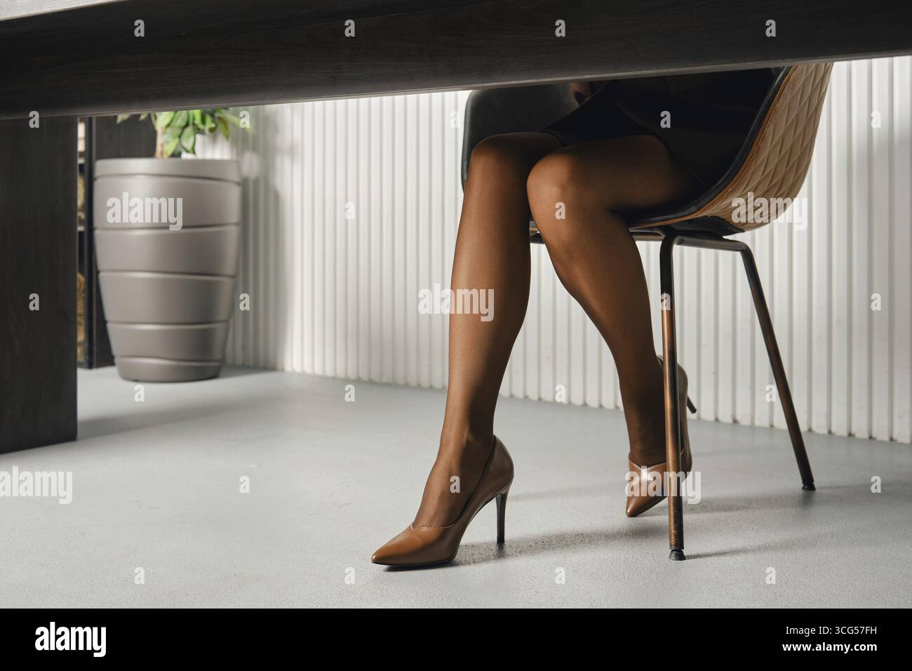 Gambe femminili sottili con collant abbronzato su una scrivania in un ufficio contemporaneo, con eleganti tacchi alti Foto Stock