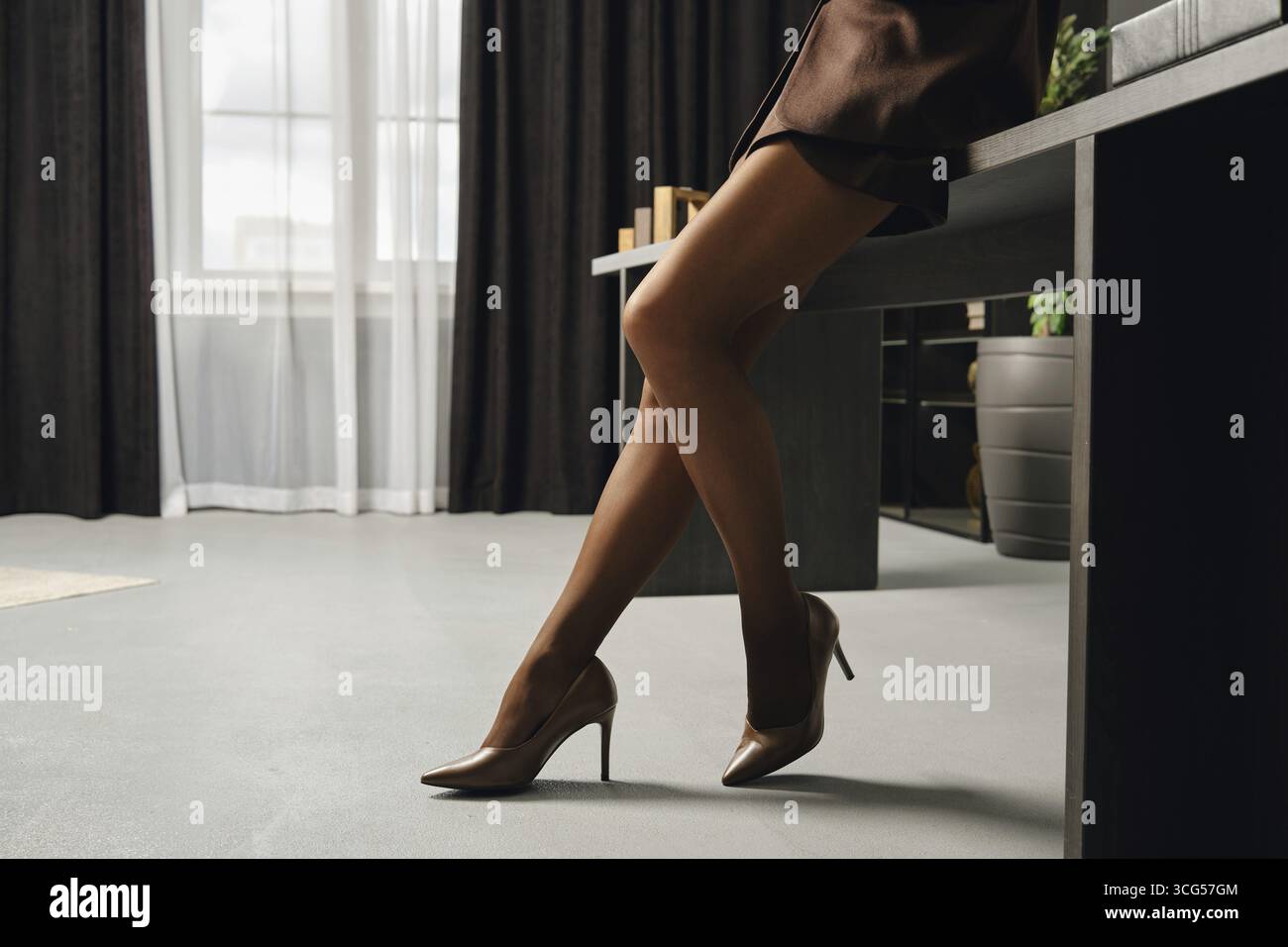 Una donna indossa elegantemente i tacchi alti, mostrando le sue gambe in collant marrone e scarpe con tacco alto marrone Foto Stock