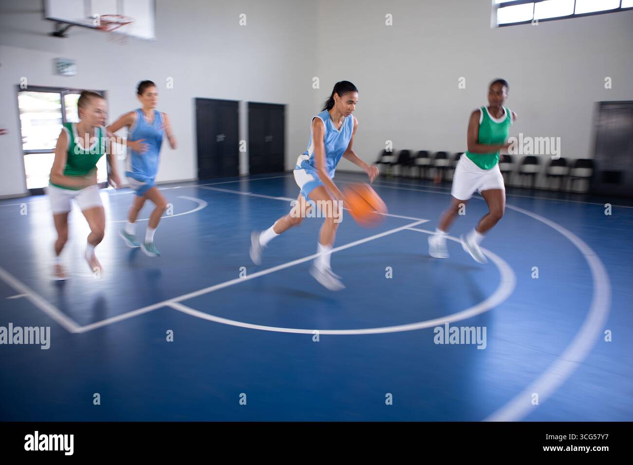 Diverse giocatrici che giocano a pallacanestro sotto il cerchio su un arco a 3 punti in palestra con sedie pieghevoli Foto Stock
