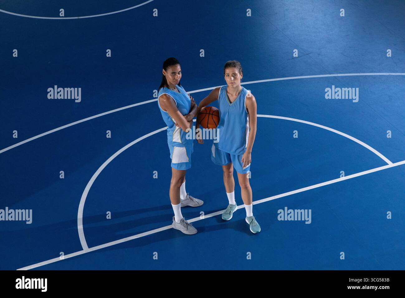 Compagni di squadra femminili di basket in piedi sul campo blu con linee che tengono la palla sotto il braccio rivolto verso l'alto Foto Stock