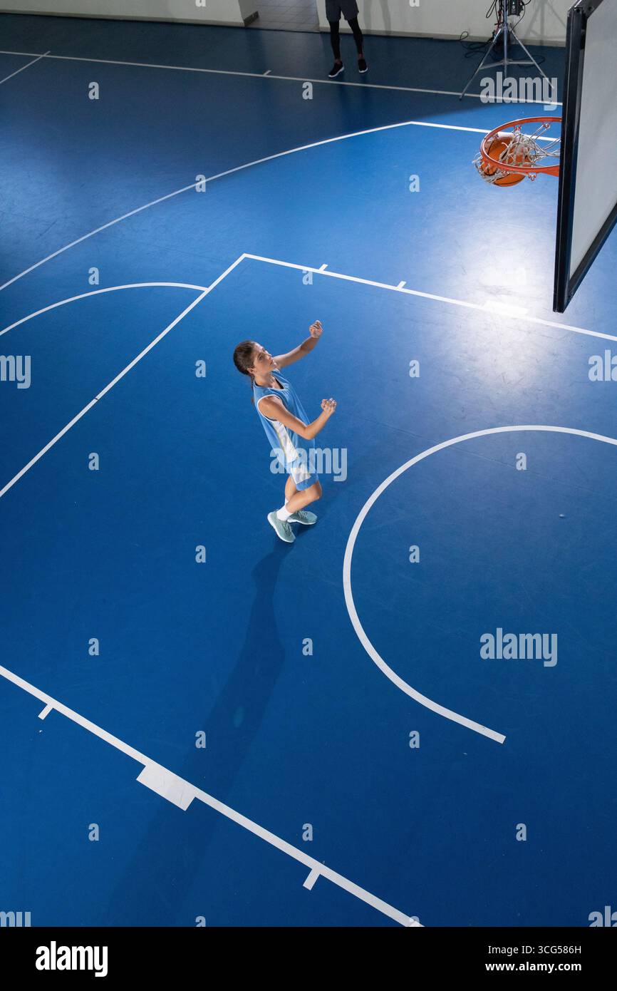 Donna in piedi sul campo da basket blu che indossa una maglia rivolta verso il canestro con il canestro sul bordo Foto Stock