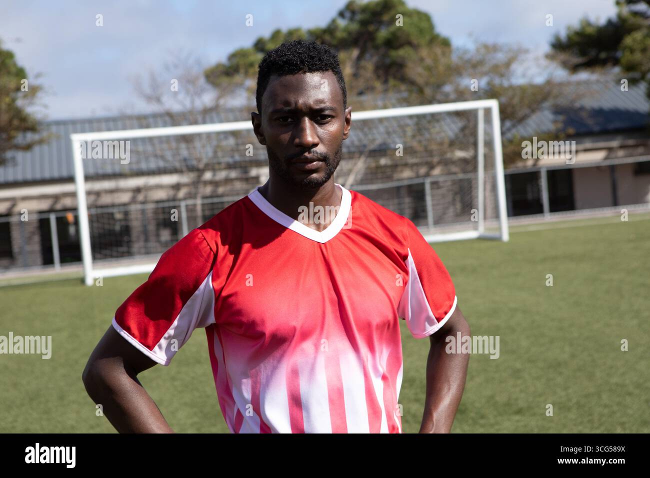 Giocatore di calcio afroamericano maschile in piedi con le mani sui fianchi su erba artificiale vicino alla rete porta Foto Stock