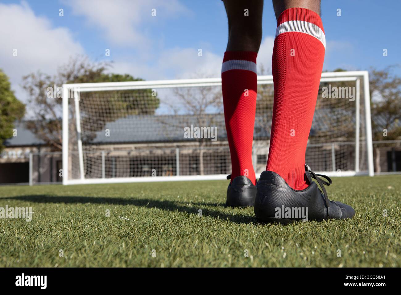 Uomo afroamericano in piedi sul campo di erba davanti a porta con calzini e scarpe rosse, copia spazio Foto Stock