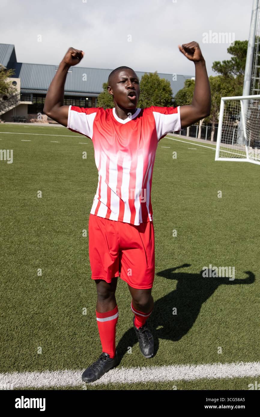 Uomo afroamericano che festeggia sul campo artificiale in maglia rossa e bianca per rete Foto Stock