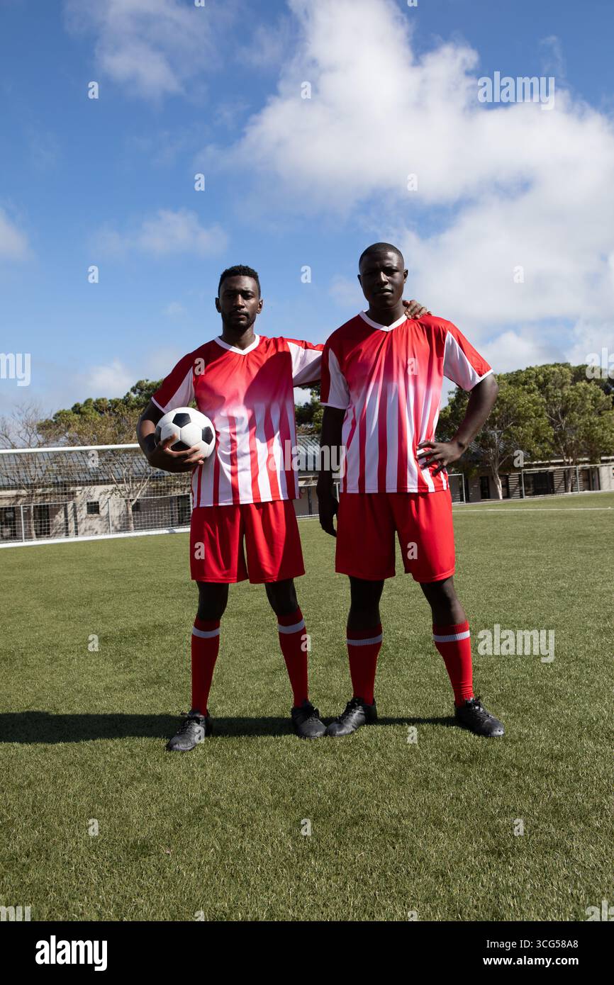 Due giocatori di calcio afroamericani maschili in maglie rosse in piedi sul campo tenendo palla con rete Foto Stock