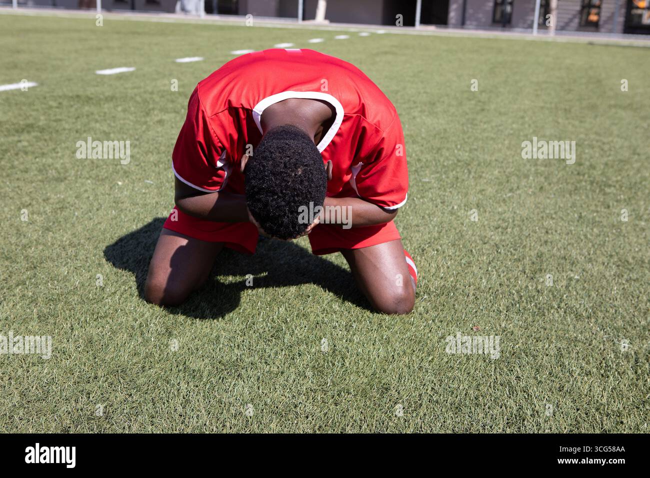 Uomo afroamericano giocatore di calcio inginocchiato tenendo la testa sul prato verde con segni bianchi Foto Stock